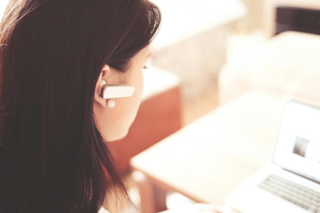 zipwp image 210647 A businesswoman using a Bluetooth headset while working on her laptop in a modern office.